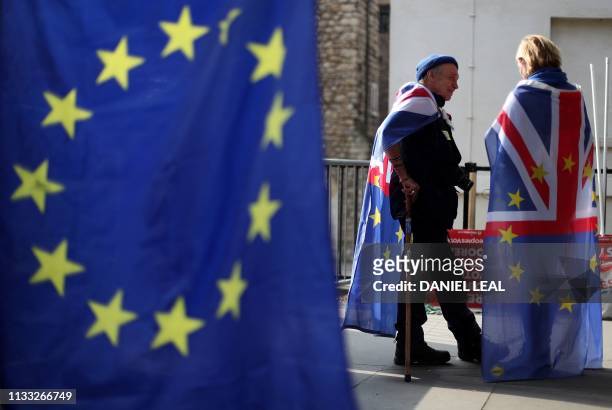 Anti-Brexit activists draped in Union and EU themed flags talk during a demonstration near the Houses of Parliament in Westminster, London on March...