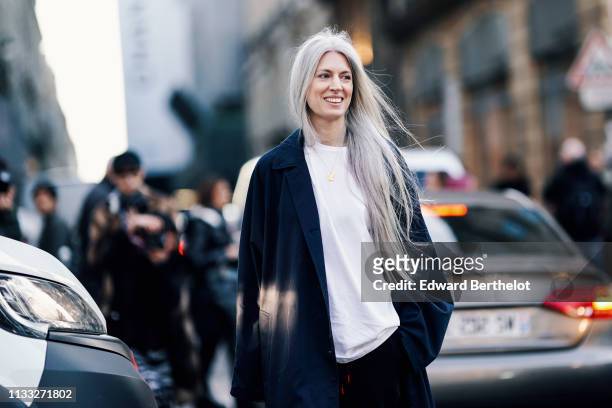 Sarah Harris wears a white t-shirt, a long dark jacket, black pants, white shoes, outside CDG Comme des Garcons, during Paris Fashion Week Womenswear...
