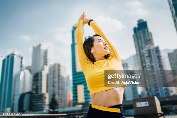 confidence and determined sports woman stretching arms over head outdoors against urban cityscape - self improvement stock pictures, royalty-free photos & images