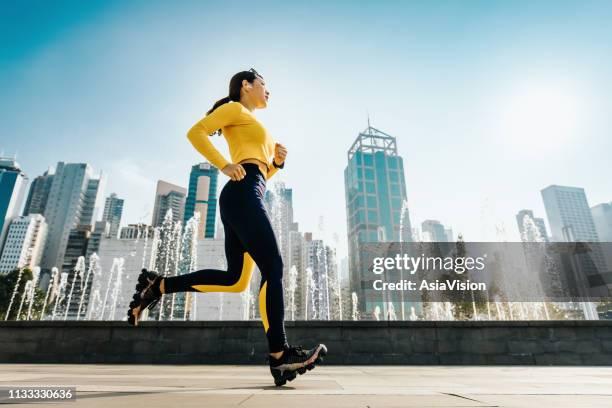 ung kvinnlig jogger kör i stads parken i staden, med modern stadssilhuett som bakgrund - asian exercise bildbanksfoton och bilder