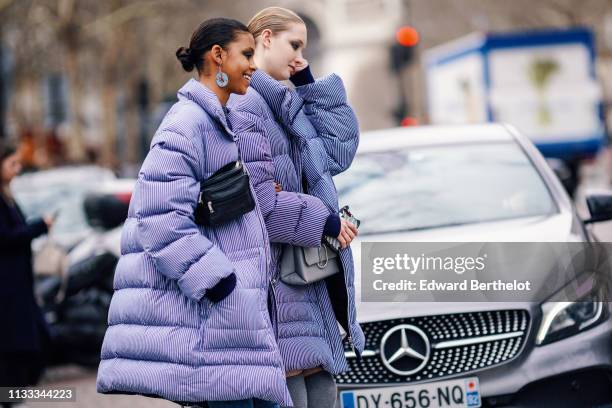 Model wears earrings, a black bag, a purple striped puffer coat ; a model wears a grey bag, a blue striped puffer coat, outside Altuzarra, during...