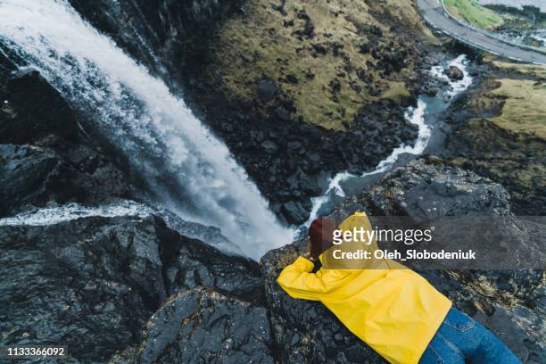 vrouw in gele regenjas staande in de buurt van de waterval in de faeröer - faroe islands stockfoto's en -beelden