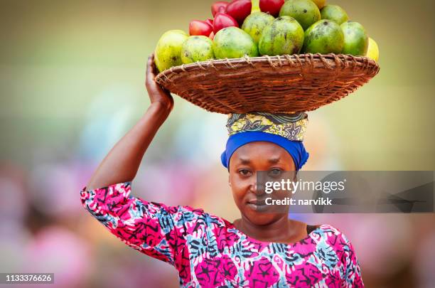 mujer rwanesa llevando cesta llena de frutas - africano fotografías e imágenes de stock