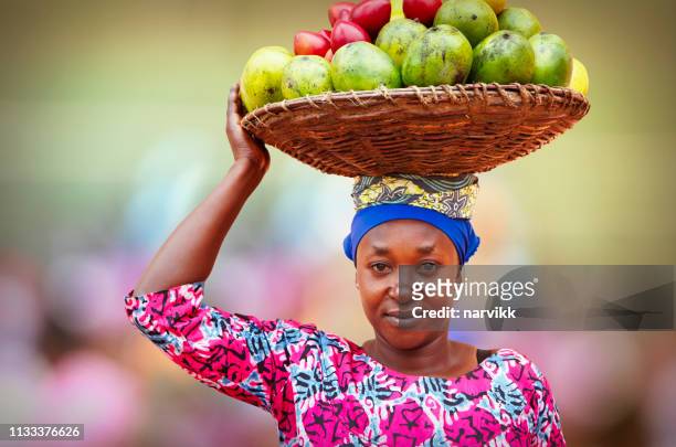 donna ruandese che porta un cesto pieno di frutta - african foto e immagini stock