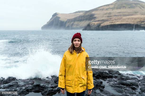 vrouw in gele regenjas wandelen in de buurt van de zee in de faeröer - faroe islands stockfoto's en -beelden