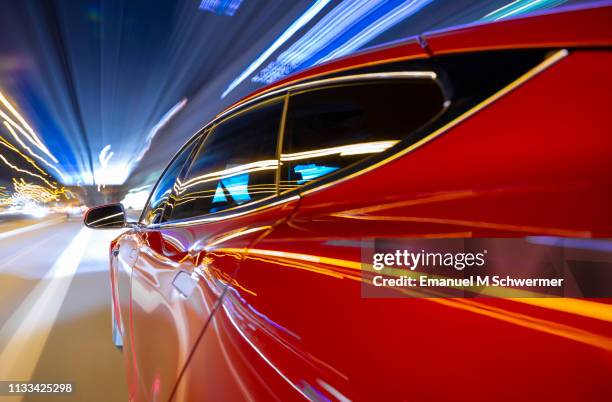 red electric powered car drives on city highway while night - streaking street lights and signs. - luxeauto stockfoto's en -beelden