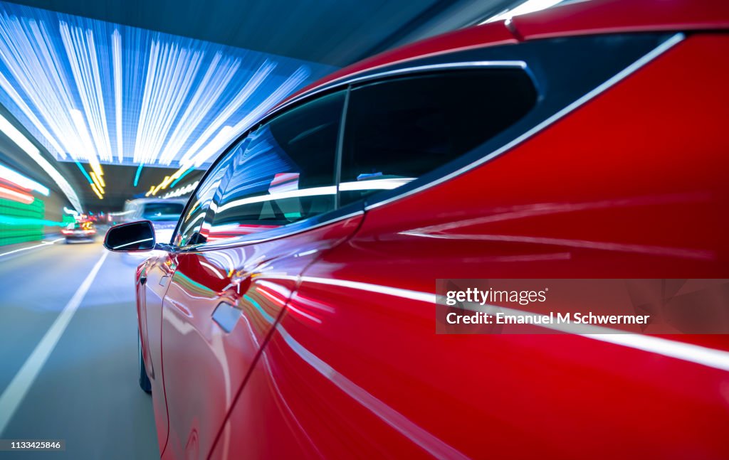 Electric powered red e-car drives on city highway while night - street lights and illuminated signs streaking.