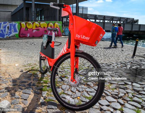 Couple walks by a parked Uber-Jump electric bicycle on the Ciclovia Lisboa Cidade by Tagus Ricer in Cais Gás on March 03, 2019 in Lisbon, Portugal....