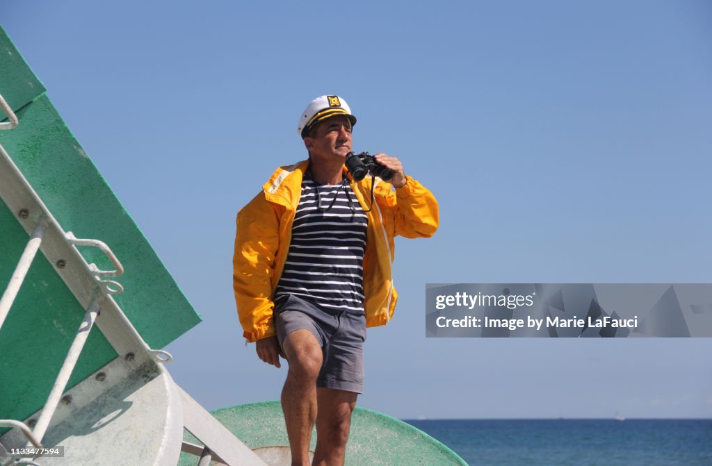 Handsome boat captain standing on a channel marker holding binoculars