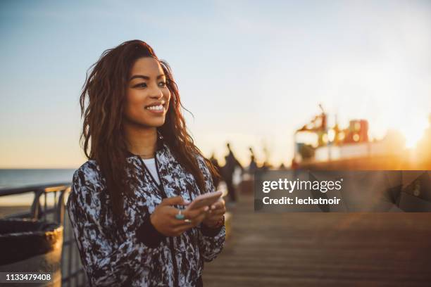 joven mujer de moda mensajes de texto en su teléfono en santa mónica, la - california beach fotografías e imágenes de stock