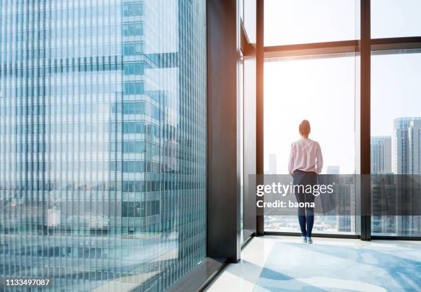 woman standing and looking at cityscape - business woman looking through window stock pictures, royalty-free photos & images