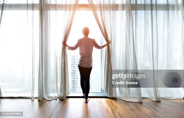 woman opening curtains and looking out - opening the curtains stock pictures, royalty-free photos & images