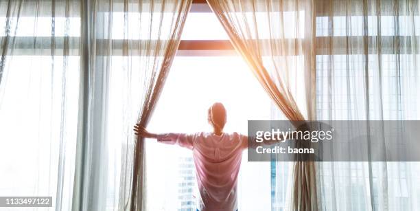 donna che apre tende e guarda fuori - mattina foto e immagini stock