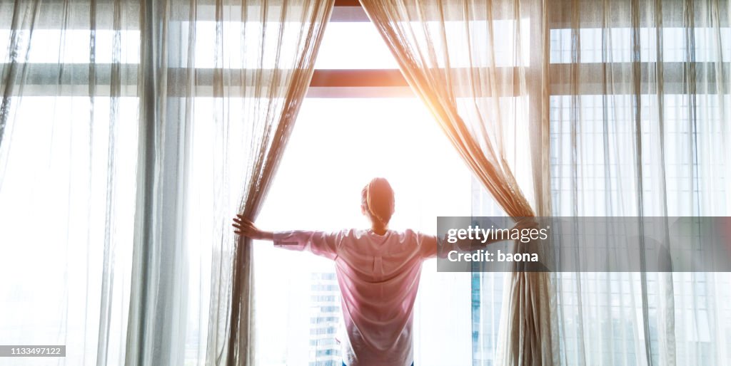 Woman opening curtains and looking out