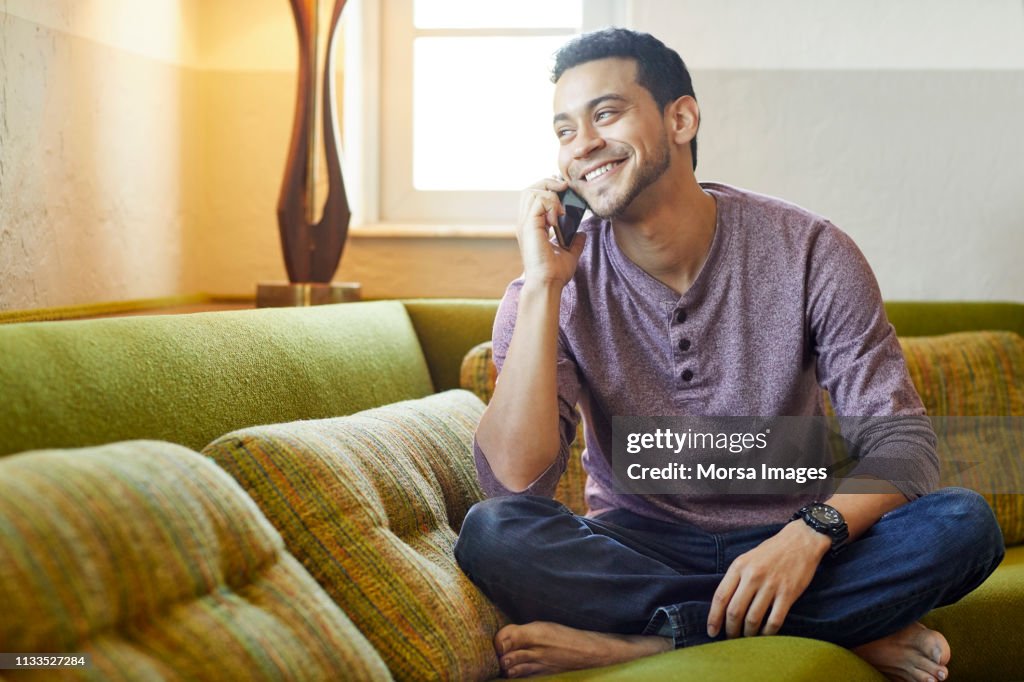 Smiling young man answering smart phone on couch