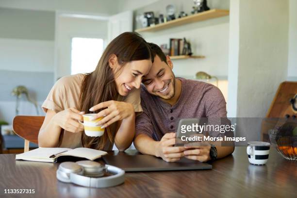 cheerful couple using mobile phone in dining room - cheerful stock pictures, royalty-free photos & images