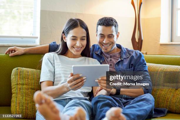 smiling young couple using digital tablet at home - young couple on couch stock pictures, royalty-free photos & images