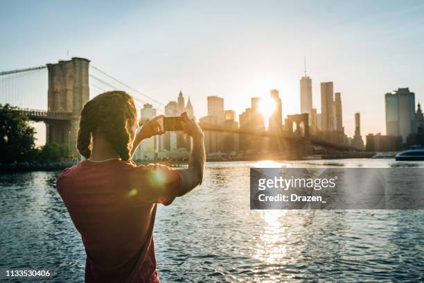 afro-caribbean, hispanic tourist in new york, taking shot of manhattan in sunset - afro caribbean and american stock pictures, royalty-free photos & images