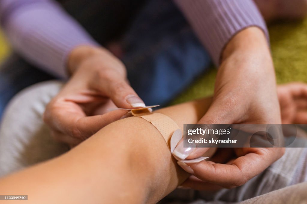 Close up of woman putting adhesive bandage on child's elbow.