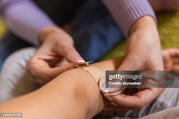 close up of woman putting adhesive bandage on child's elbow. - applying bandage stock pictures, royalty-free photos & images