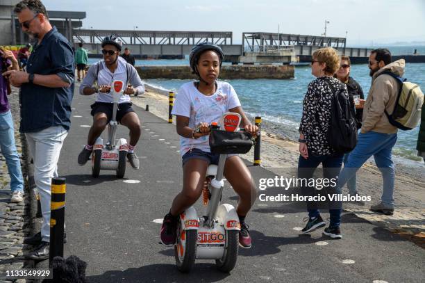 Tourists pass by pedestrians while riding Sitway concept e-scooters on the Ciclovia Lisboa Cidade by Tagus River in Cais Gás on March 03, 2019 in...