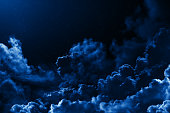 Mystical midnight sky with stars surrounded by dramatic clouds. Dark natural background with night starry cloudy sky. Moonlit clouds