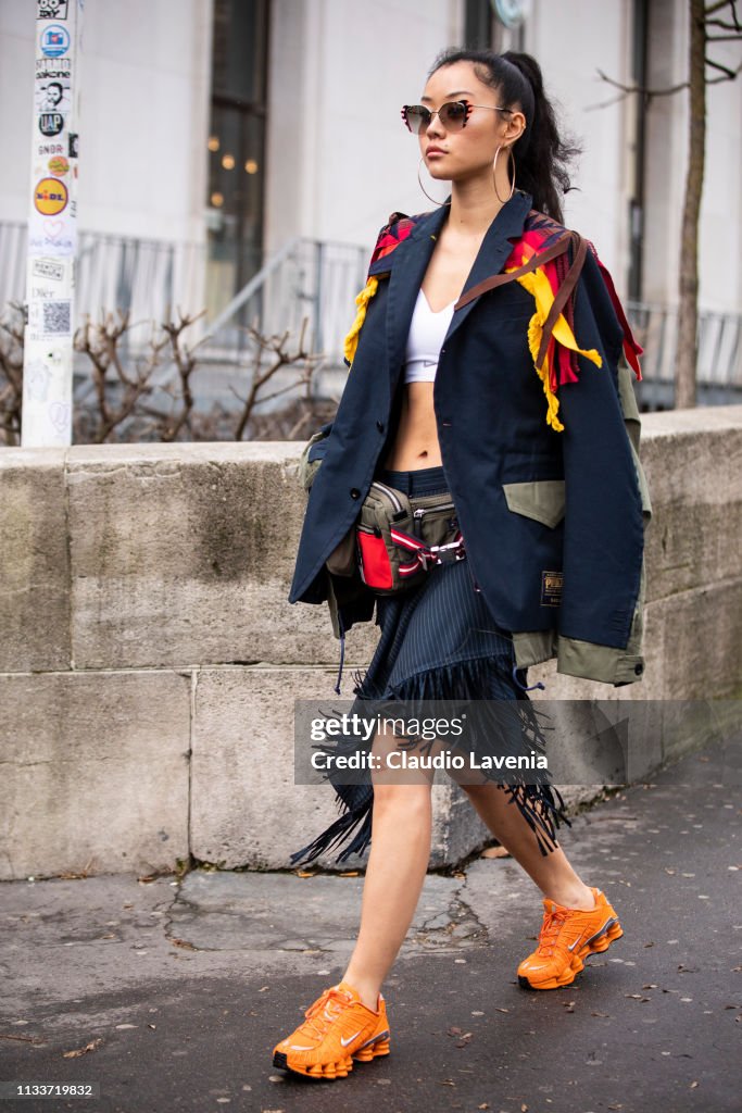 A guest, wearing a colorful decorated jacket, blue skirt, white crop ...