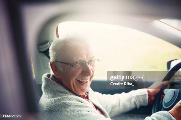 el viejo caballero conduce el coche y ríe en la cámara fotográfica - autos usados fotografías e imágenes de stock