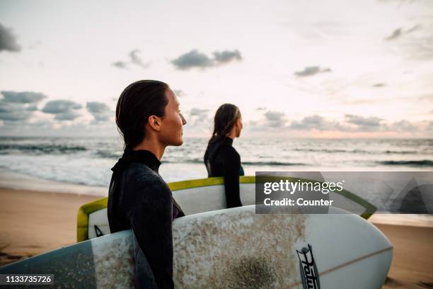 two female surfers with surfboards on beach at sunset - biarritz 個照片及圖片檔