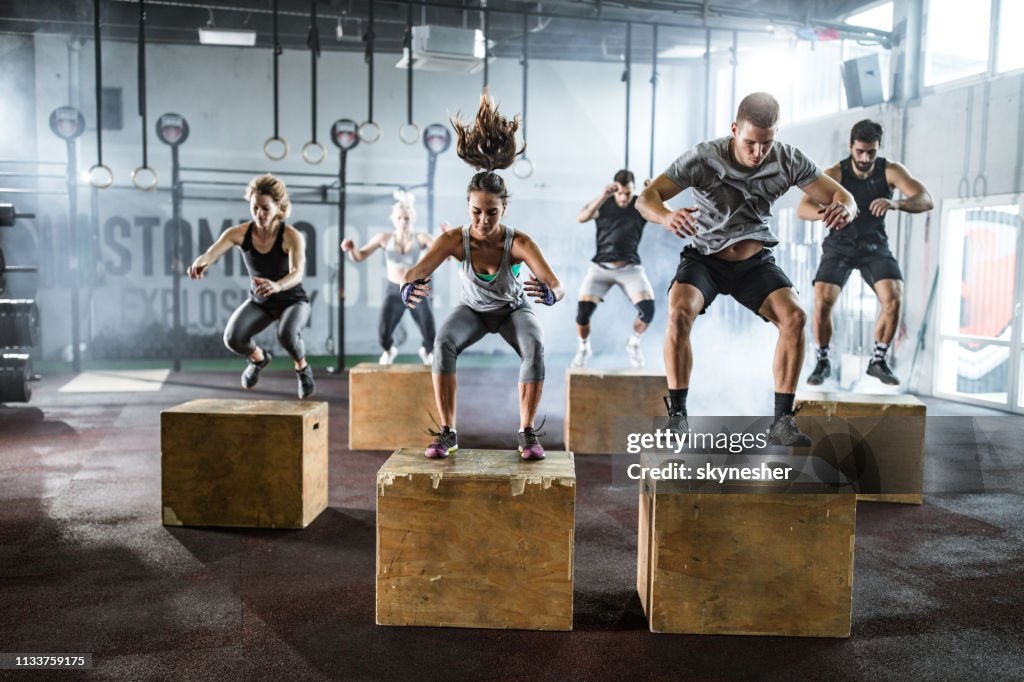 Athletic people jumping on crates during cross training in a health club