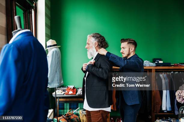 retail assistant helping customer trying on a jacket - bespoke stock pictures, royalty-free photos & images