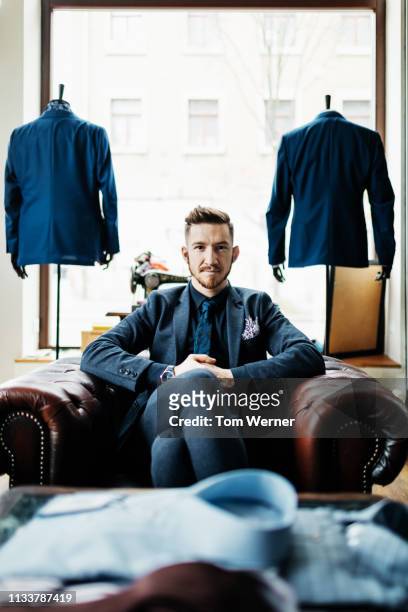 portrait of menswear store owner sitting in armchair - tailored suit stock pictures, royalty-free photos & images