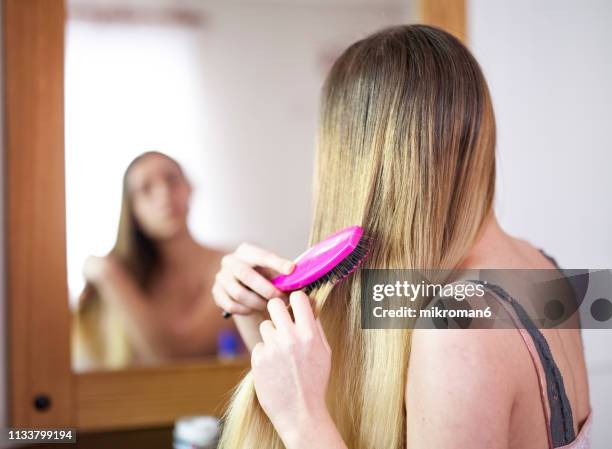 young woman brushing her hair looking into a mirror - woman brushing hair stockfoto's en -beelden