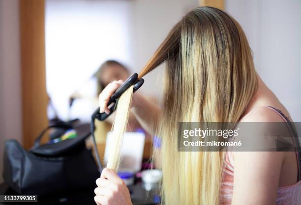 young woman straightening her hair while looking into a mirror - blusher foto e immagini stock