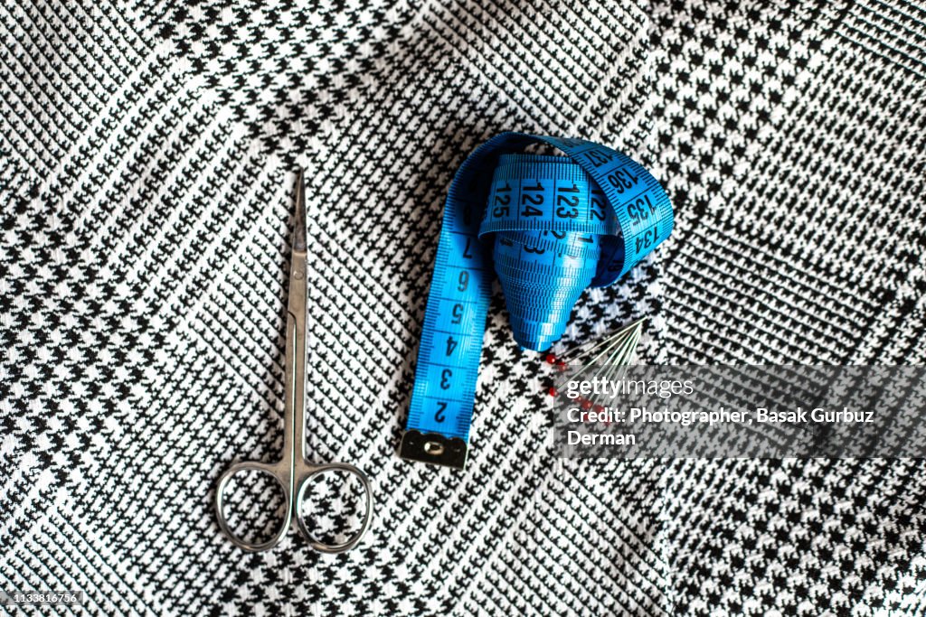Sewing items; fabric, tape measure, ball head sewing needles, and scissors.
