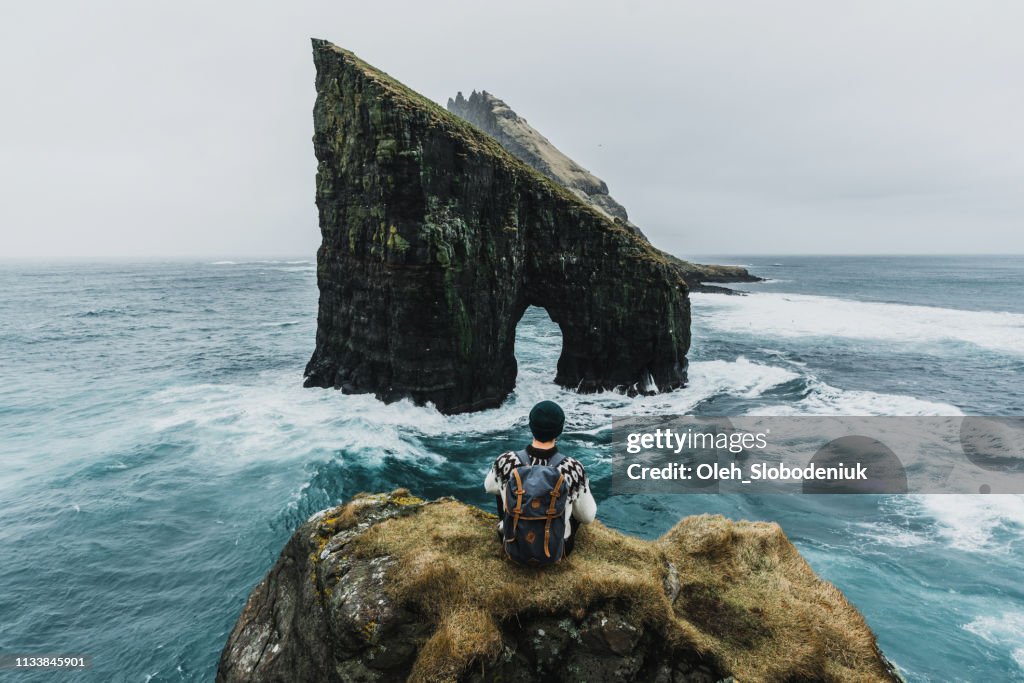 Man in knitted sweater looking at view of Drangarnir arch in Faroe Islands