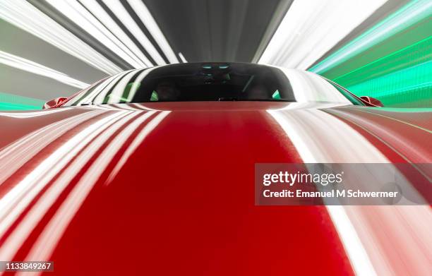 electric powered red us car drives through tunnel with streaking lights on the hood of the car. - shiny car stock pictures, royalty-free photos & images