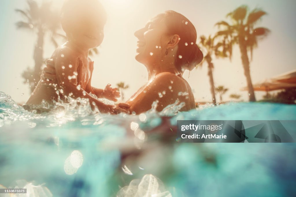Madre con bambino che si diverte in piscina al tramonto