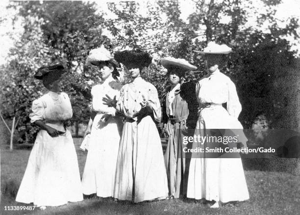 Five young women, wearing Edwardian dresses and hats, pose together in a garden setting, including future First Lady Bess Truman nee Wallace likely...