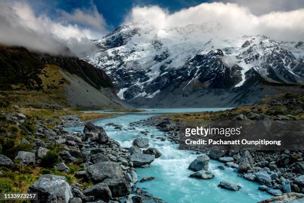 view of river in front of snowcapped mountain with some clouds on some part of top mountain at hooker valley track in aoraki/mount cook national park, new zealand - christchurch new zealand stock-fotos und bilder