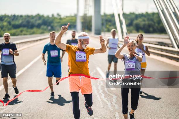 senior marathon runners celebrating his victory while crossing the finish line. - man-crossing-finish-line-in-running-race stock pictures, royalty-free photos & images