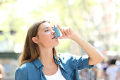 Asthmatic woman using inhaler standing in the street