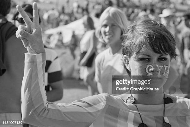 Woman, with word 'Love' painted on her face, makes peace sign at a love-in held at Griffith Park, Los Angeles, US, 1967.