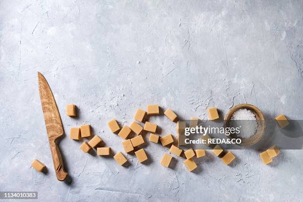 Salted caramel fudge candy served with fleur de sel in wooden bowl and knife over grey texture background Top view, copy space.