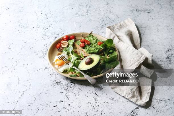 Vegetarian sandwiches with avocado, poached egg, spinach, cherry tomatoes on whole grain toast bread on ceramic plate with textile napkin over white...