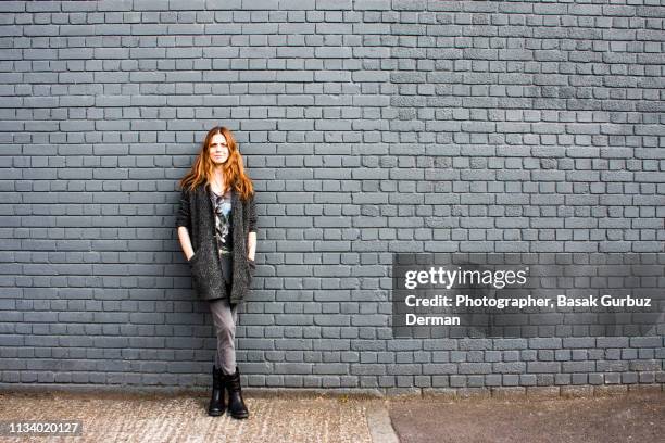 portrait of a young and confident woman leaning against a brick wall - gray jeans stockfoto's en -beelden