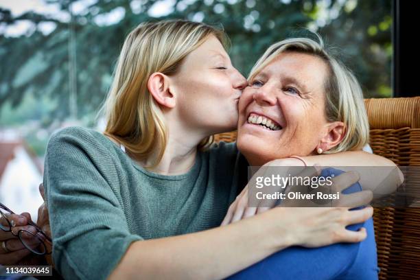 happy senior woman and young woman hugging and kissing in armchair - daughter stock-fotos und bilder