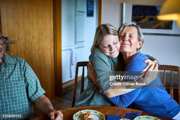 adult granddaughter and grandmother hugging at dining table - visit grandmother stock pictures, royalty-free photos & images