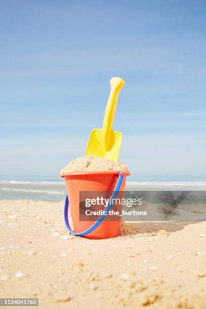 still life of red bucket and yellow shovel on the beach against sky - emmer stockfoto's en -beelden