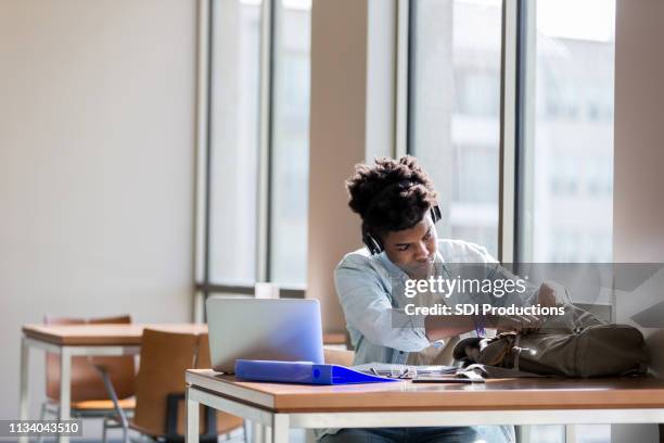 teen boy studies in school library with headphones - open backpack stock pictures, royalty-free photos & images